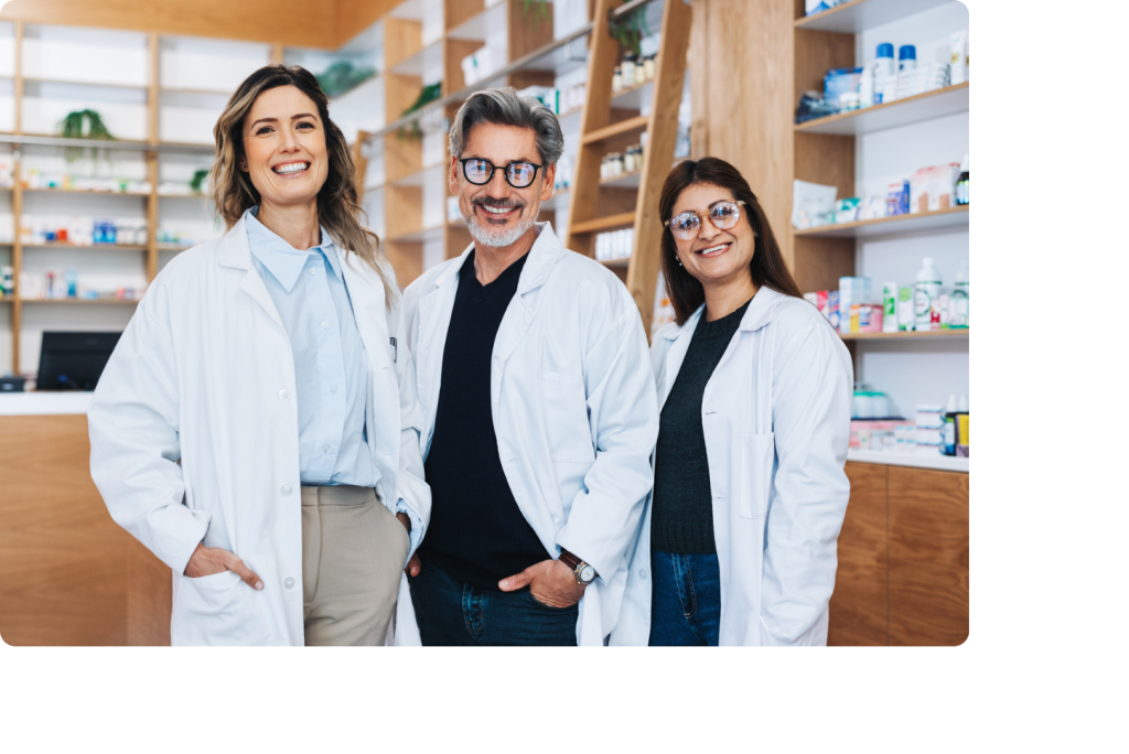 Trois personnes d'une équipe officinale en blouse souriant au milieu d'une pharmacie