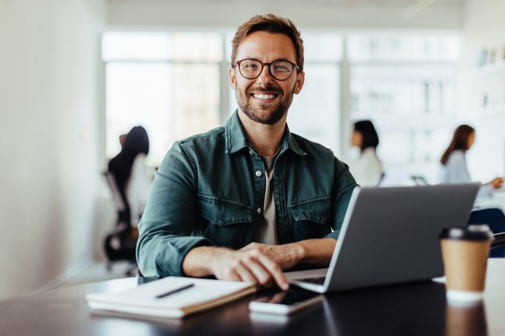 Homme souriant assis à un bureau travaillant sur un ordinateur portable