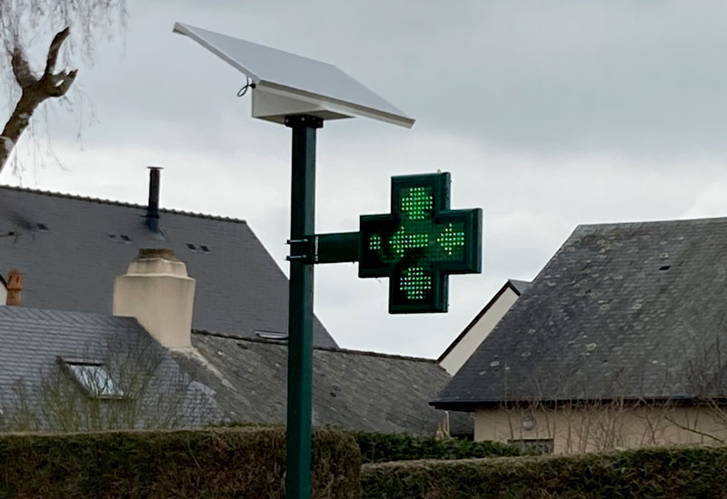 Croix de pharmacie solaire sur un poteau dans la rue