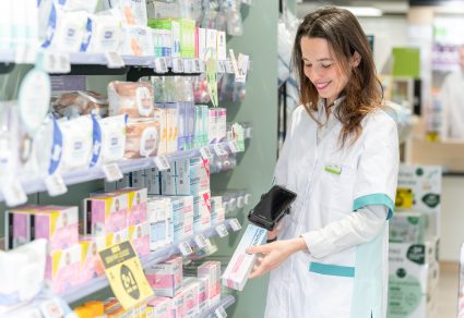 Pharmacienne en blouse blanche qui scanne un produit dans un rayon avec la solution Smart Rx Logi Stock