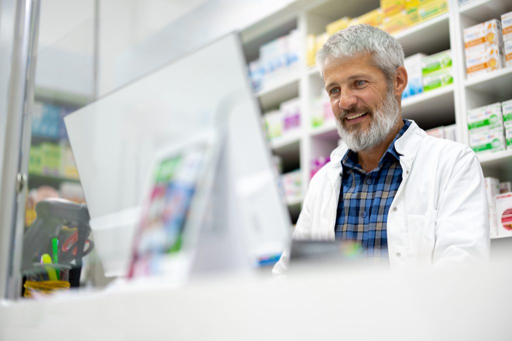 Pharmacien en blouse blanche au comptoir devant son poste informatique