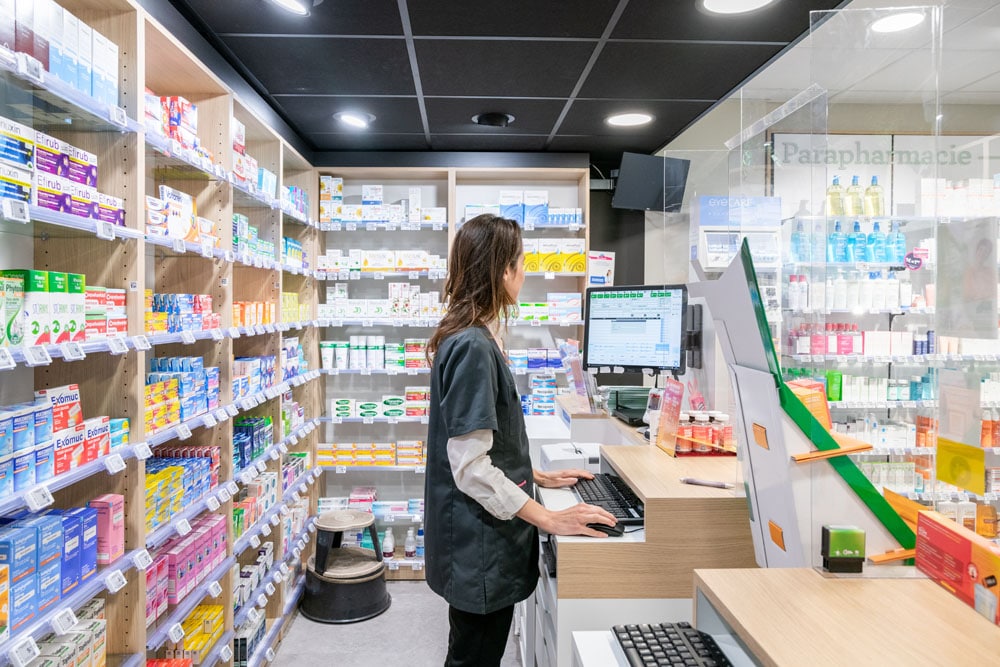 Photo prise de l'arrière du comptoir de l'officine avec un pharmacien en action devant le LGO